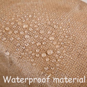 May include: Close-up of a tan, textured fabric with water droplets on the surface. The words "Waterproof material" are written in white at the bottom of the image. The fabric appears to be water-resistant.