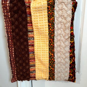 May include: A rectangular tote bag constructed from vertical fabric strips in various textures and patterns, including brown plaid, solid brown tufted fabric, multicolored stripes, yellow textured fabric, orange and green polka dots, and cream chenille.
