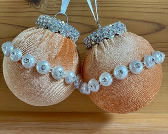 Può includere: Due addobbi natalizi in velluto color pesca con bordino di perle bianche e dettagli in strass argentati.