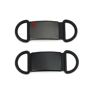 Op de afbeelding: Twee zwarte medische ID-tags met een rood ster-van-leven-symbool op één tag. De tags hebben aan elk uiteinde een zwarte rubberen lus.