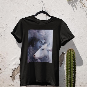 Könnte beinhalten: Schwarzes T-Shirt mit einem grafischen Druck einer blauhäutigen Gottheit, die ein weißes Tier hält. Die Gottheit trägt einen blauen Kopfschmuck und hat einen sanften Ausdruck.
