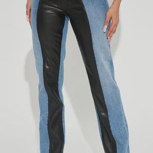 Könnte beinhalten: Hose mit hoher Taille und Color-Blocking-Design, bestehend aus hellblauen Denim-Seitenteilen und einem breiten, vertikalen schwarzen Kunstlederstreifen in der Mitte jedes Beins, inklusive klassischem Knopfverschluss und Gürtelschlaufen.