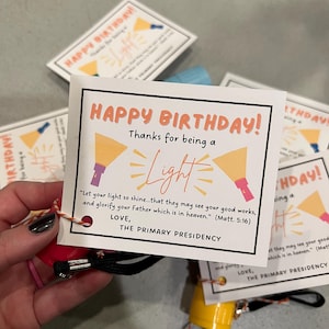 May include: Birthday cards with the text "Happy Birthday! Thanks for being a Light." The cards have a flashlight graphic and a quote from Matthew 5:16. Each card is attached to a small flashlight.