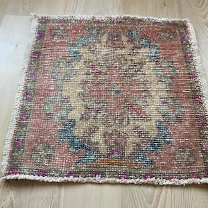 May include: A small, pink and beige rug with a floral pattern. The rug has a fringed edge.