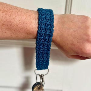 May include: A dark blue crocheted key chain with a silver key ring and a key attached.