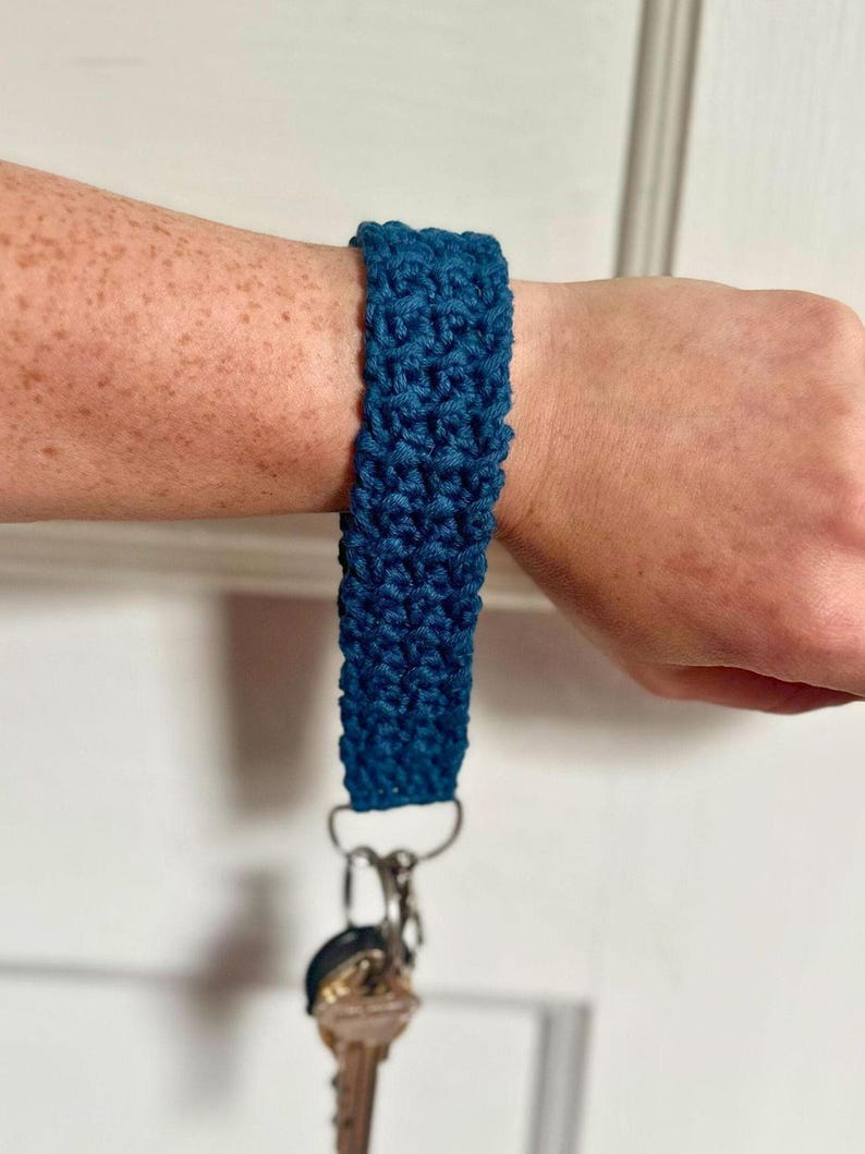 May include: A dark blue crocheted key chain with a silver key ring and a key attached.
