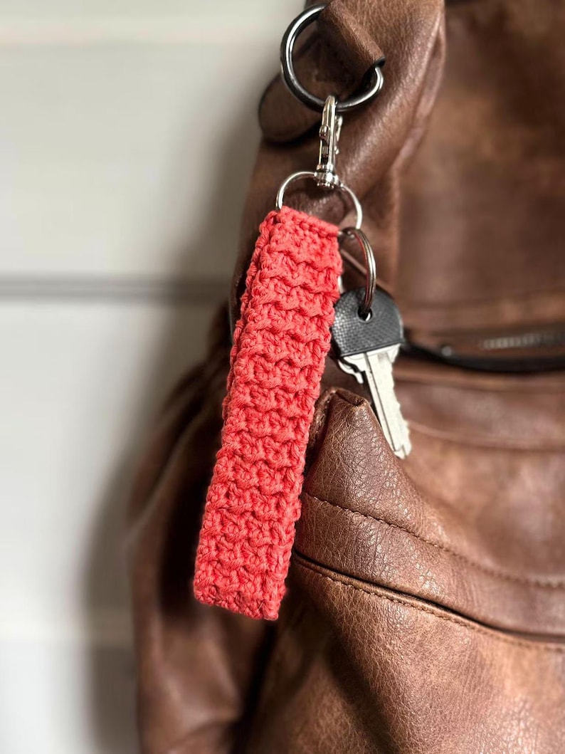 May include: A red crocheted keychain attached to a brown leather bag with silver key rings and keys.