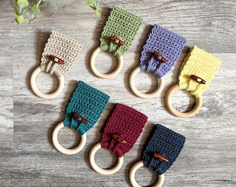 May include: Seven crocheted teethers in various colors, including green, purple, yellow, teal, maroon, and navy blue, attached to wooden rings. Each teether has a wooden button.