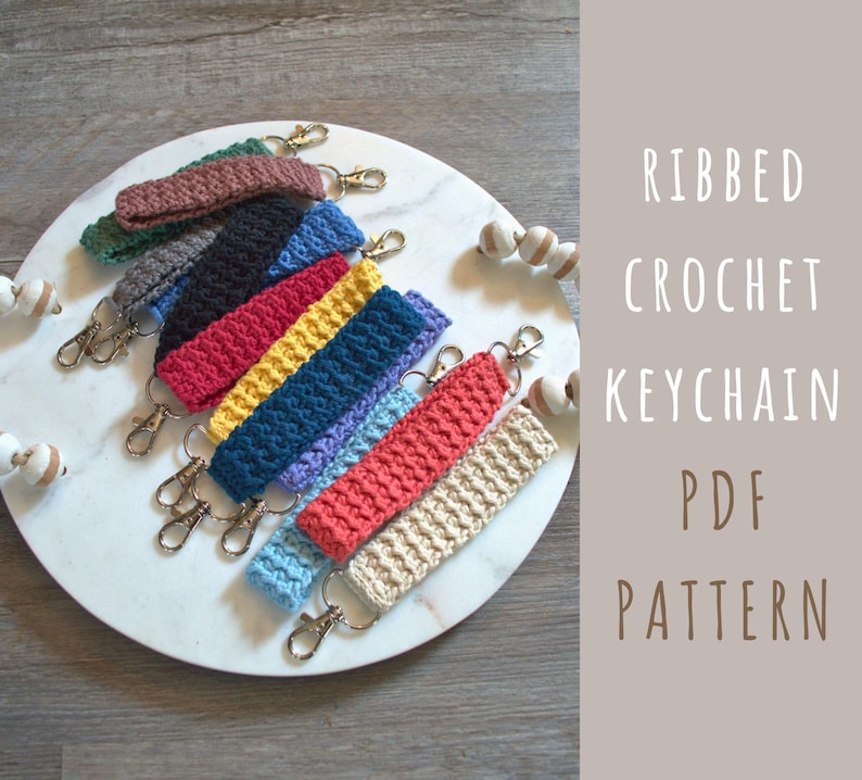 May include: A collection of colourful crocheted keychain straps with metal key rings. The keychains are made with a ribbed stitch pattern. The image includes the text "RIBBED CROCHET KEYCHAIN PDF PATTERN".