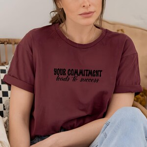 May include: A maroon t-shirt with the text "YOUR COMMITMENT leads to success" printed in black.