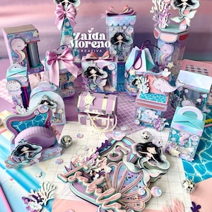 Op de afbeelding: Een verzameling feestdoosjes en decoraties met illustraties van zeemeerminnen en zeedieren in pastelblauw, paars en roze. De items bevatten doosjes met strikken, een schatkist en een centerpiece met de naam Isabella en het cijfer 5.