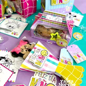 Peut inclure: Une collection de bo&icirc;tes cadeaux, d'&eacute;tiquettes et d'autocollants color&eacute;s avec le texte "Feliz D&iacute;a del Ni&ntilde;o" et des visages souriants. Les bo&icirc;tes contiennent des biscuits et d'autres friandises. La palette de couleurs comprend le rose, le jaune et le violet.