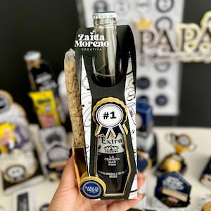 May include: A gift set featuring a bottle of Extra beer, a bag of peanuts, and decorative elements. The beer bottle is in a black and white gift box with a gold-trimmed label that reads "#1" and "Extra". The gift set is labeled "Para el Mejor".