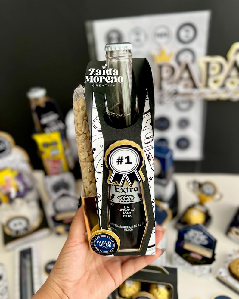 May include: A gift set featuring a bottle of Extra beer, a bag of peanuts, and decorative elements. The beer bottle is in a black and white gift box with a gold-trimmed label that reads "#1" and "Extra". The gift set is labeled "Para el Mejor".