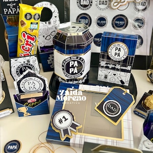 May include: An assortment of Father's Day gifts, including a can-shaped container, gift boxes, and tags. The items feature blue and gold accents, with text that reads "DAD" and "PA PA". There is also a candy bar.