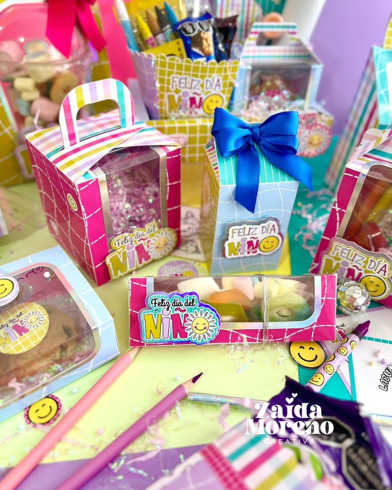 Peut inclure: Une collection de bo&icirc;tes cadeaux et de contenants color&eacute;s, certains avec des fen&ecirc;tres transparentes, remplis de friandises. Les bo&icirc;tes sont d&eacute;cor&eacute;es de rayures, de n&oelig;uds et du texte "Feliz D&iacute;a del Ni&ntilde;o" et un soleil souriant. Des crayons et des autocollants smiley sont &eacute;galement visibles.