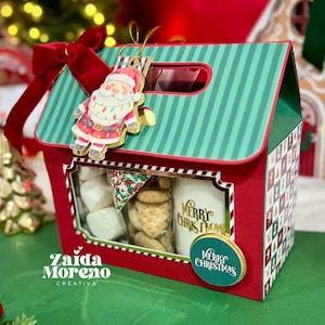 May include: A festive Christmas gift box in red and green, adorned with a Santa Claus decoration and a red velvet bow. Inside, the box holds marshmallows, biscuits, and a mug with "Merry Christmas" written on it.