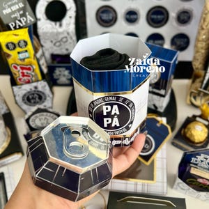 May include: A gift set for Father's Day, featuring a cylindrical container with a blue and white design, filled with black socks. The set includes a can-shaped box, tags, and other decorative elements with the word "DAD" and "PAPA".