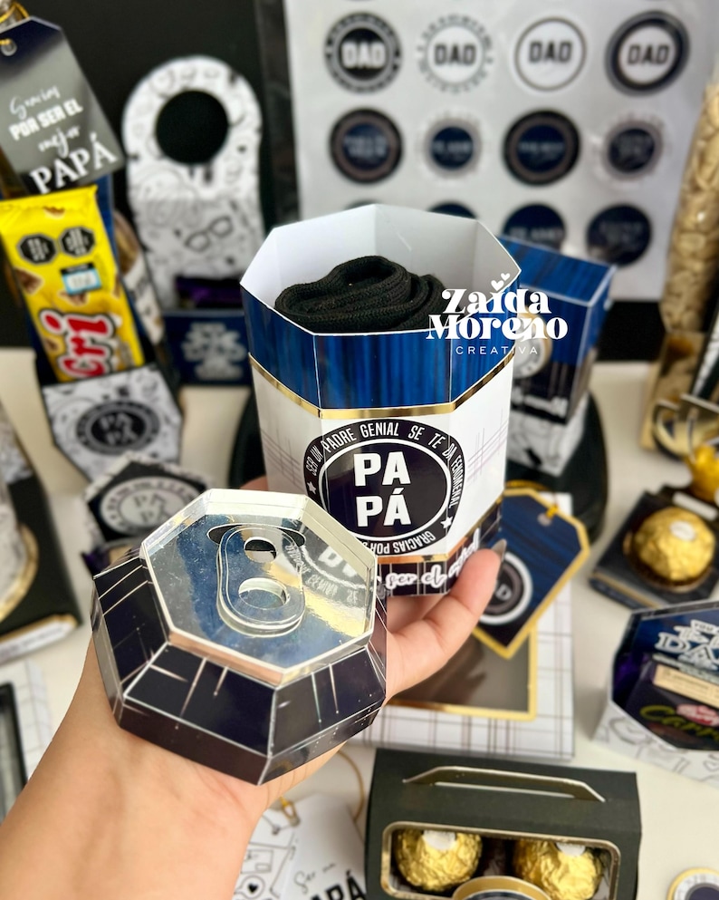 May include: A gift set for Father's Day, featuring a cylindrical container with a blue and white design, filled with black socks. The set includes a can-shaped box, tags, and other decorative elements with the word "DAD" and "PAPA".