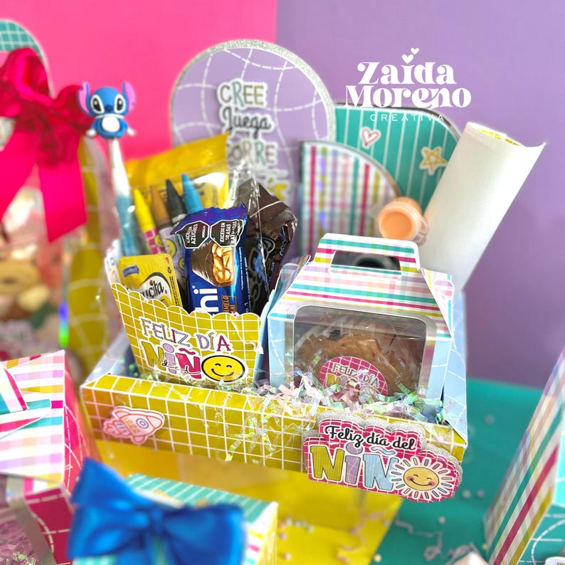 Peut inclure: Un panier cadeau color&eacute; rempli de friandises et de fournitures scolaires. Le panier comprend une bo&icirc;te de biscuits, des bonbons, des crayons et un stylo avec un personnage Stitch. Les mots "Feliz D&iacute;a del Ni&ntilde;o" sont visibles.