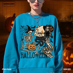 May include: A turquoise blue Halloween-themed sweatshirt with a graphic design featuring skeletons, playing cards, bats, and a pumpkin. The word "HALLOWEEN" is printed in bold letters at the bottom of the design. The brand name "MONOLINES" is at the top.