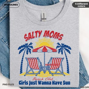 K&ouml;nnte beinhalten: Ein graues T-Shirt mit einem rot-wei&szlig;-blauen Grafikdesign. Die Grafik zeigt den Text "Salty Moms Beach Club Girls Just Wanna Have Sun" mit einer Palme, Strandst&uuml;hlen und einem Sonnenschirm.