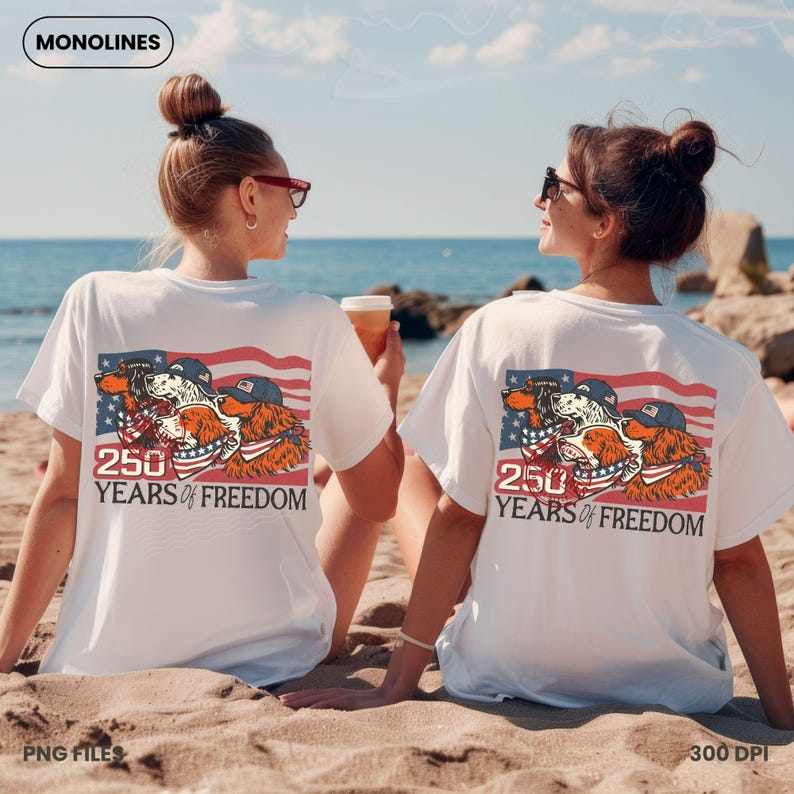 May include: White t-shirts with a graphic of three dogs in patriotic attire, set against an American flag design. The text "250 YEARS OF FREEDOM" is below the graphic. The image is on a beach with two people.