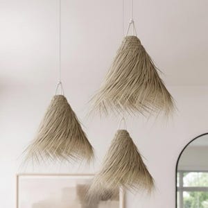 May include: Three pendant lights with natural, beige-colored woven shades hang from the ceiling. The shades have a conical shape with a fringed, textured appearance. The lights are suspended by thin, white cords, creating a minimalist, bohemian aesthetic.