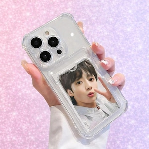 May include: Clear phone case with a photo of a person in a light blue shirt. The case has a card slot and a clear bumper. The phone case is held in a hand with manicured nails.