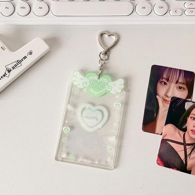 Pu&ograve; includere: Un porta tessere di plastica trasparente con un design a forma di cuore verde e ali. Il porta tessere ha una catena argentata ed &egrave; decorato con glitter e piccoli cuori. Il testo "Heart" &egrave; stampato sul cuore verde.