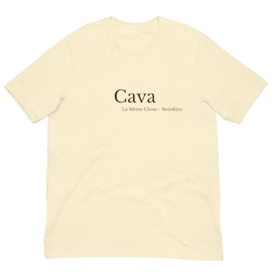May include: A cream colored t-shirt with brown text that reads "Cava La Même Chose - Brooklyn"