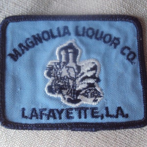 May include: Blue and white embroidered patch with the text "Magnolia Liquor Co. Lafayette, LA".