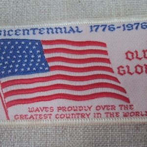 Puede incluir: Un parche blanco bordado con una bandera estadounidense roja, blanca y azul, el texto "Bicentenario 1776-1976", y las palabras "Old Glory" y "Waves proudly over the greatest country in the world".