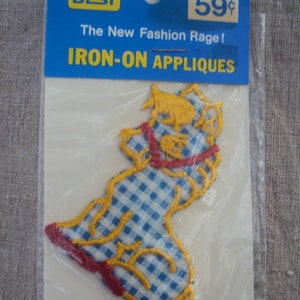 May include: Iron-on applique featuring a yellow embroidered cartoon animal wearing a blue and white gingham dress. The applique is packaged on a white card with blue text that reads "BEST The New Fashion Rage! IRON-ON APPLIQUES 59¢".