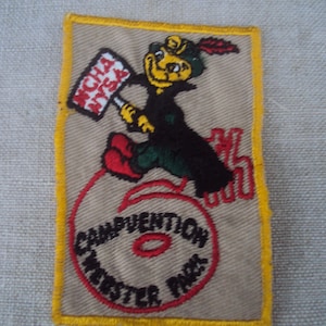 May include: A yellow, red, and black embroidered patch with a cartoon character riding a unicycle. The character is holding a sign that says "UCLA Nite". The patch says "Convention Webster Park".