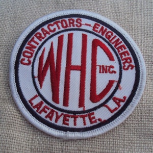 Peut inclure: Écusson brodé blanc avec un logo "WHC INC." rouge et le texte "CONTRACTORS - ENGINEERS LAFAYETTE LA" dans un cercle noir.