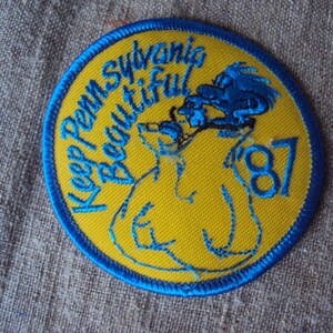 May include: A blue and yellow embroidered patch with the text "Keep Penn. Sylvannia Beautiful" and the year "1987".