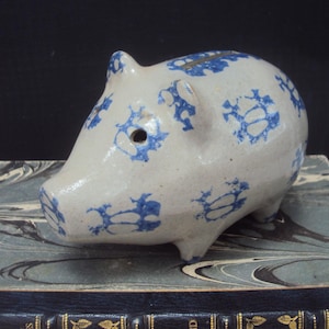 Może przedstawiać: Ceramiczna skarbonka w kolorze niebieskim i białym z niebiesko-białym wzorem kwiatowym. Skarbonka ma szczelinę na górze do wrzucania monet i otwór z boku do wyjmowania monet.