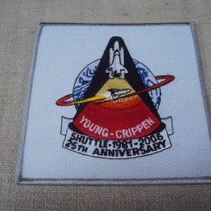 May include: A white embroidered patch with a black and red space shuttle design. The patch features the text "Young-Crippen Shuttle 1981-2006 25th Anniversary".