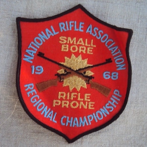 Peut inclure: Écusson brodé rouge, blanc et bleu avec le texte "National Rifle Association 1968 Regional Championship" et "Small Bore Rifle Prone" en forme de bouclier.