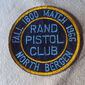 May include: A blue and gold embroidered patch with the text "Fall 1800 Match 1966 Rand Pistol Club North Bergen".