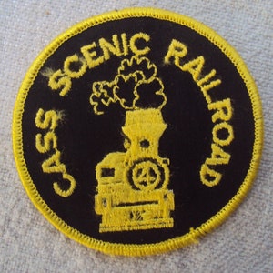 Könnte beinhalten: Ein gestickter Aufnäher in Schwarz und Gelb mit dem Text "Cass Scenic Railroad" und einem gelben Bild einer Dampflokomotive.