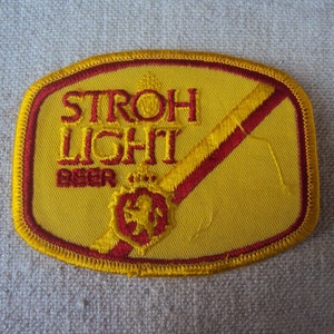 May include: A yellow and red embroidered patch with the text "STROH LIGHT BEER" and a lion logo.