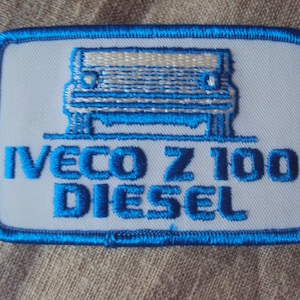 May include: A white embroidered patch with a blue border. The patch features a white cartoon truck with the text "IVECO Z 100 DIESEL" in blue.