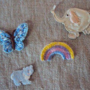 May include: Four embroidered iron-on patches: a blue butterfly, a white elephant, a rainbow, and a gray elephant. These patches are perfect for adding a whimsical touch to clothing, bags, or other fabric items.