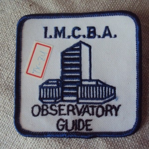 May include: A white square patch with a blue border. The patch has a blue and white building with the text "L.M.C.B.A." above it. The text "OBSERVATORY GUIDE" is below the building.