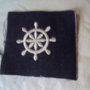 May include: A dark blue fabric patch with a white embroidered ship's wheel.