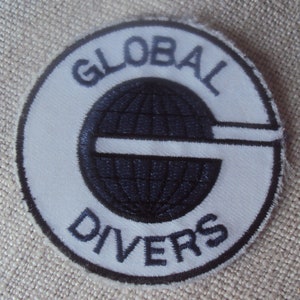 May include: White embroidered patch with a blue globe and the text "GLOBAL DIVERS" in a circle.