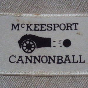 Op de afbeelding: Witte stoffen patch met zwarte geborduurde tekst en een kanon afbeelding. De tekst luidt "McKeesport Cannonball".