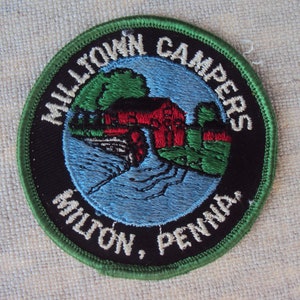 May include: Circular patch with the text "MILLTOWN CAMPERS MILTON, PENNA." The patch features a red building, green trees, and blue water. The border is green, and the background is black.